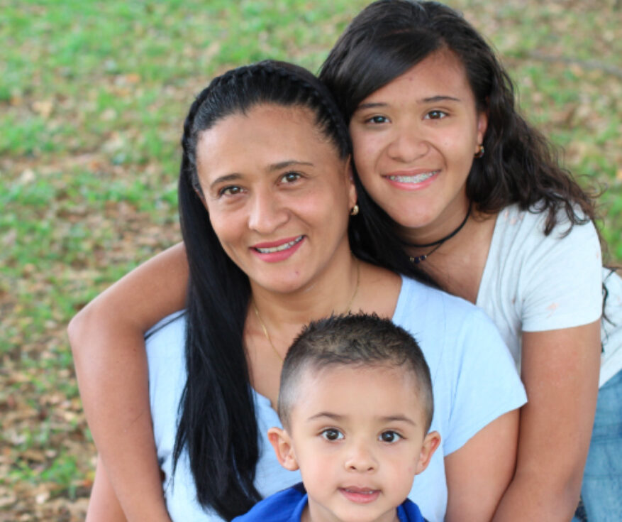 A mother and her two children smiling into the camera outdoors, reflecting the safe and supportive community provided by Operation HOPE-North County.
