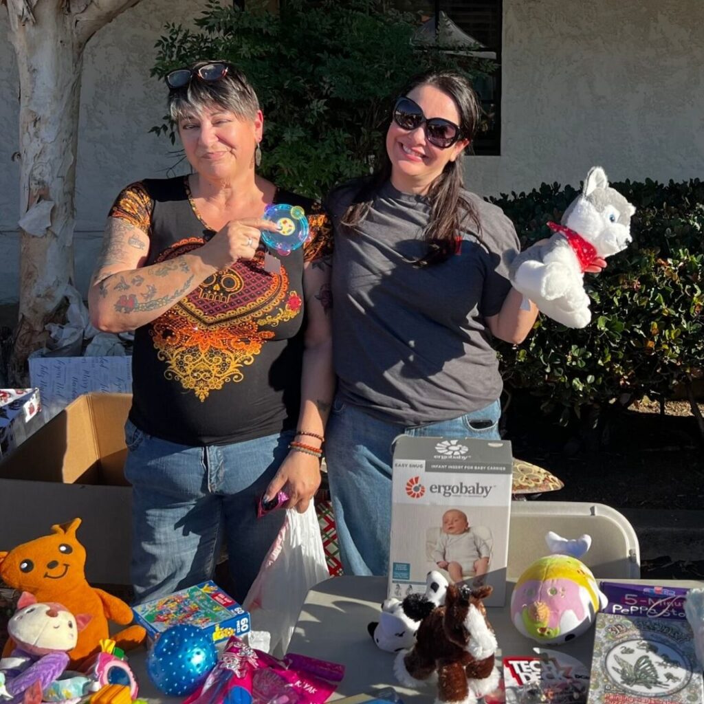 Two smiling women displaying donated toys at an OHNC shelter event table.