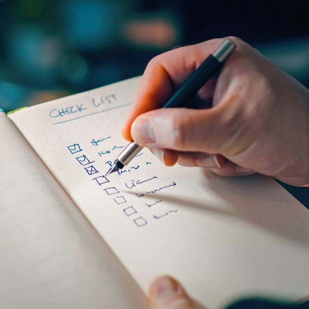 Close-up of a hand using a fountain pen to check off items on a written checklist in a notebook.