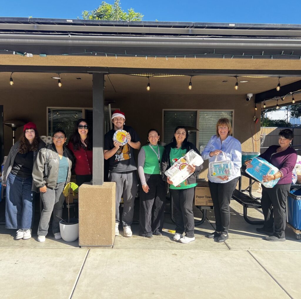 Group of smiling Operation HOPE team members and volunteers posing outdoors with donated supplies.